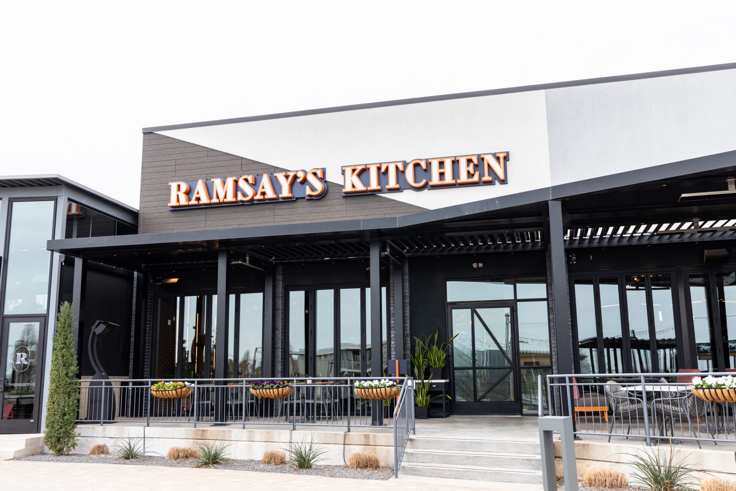 Exterior of Ramsay’s Kitchen restaurant with modern design and outdoor planters visible.