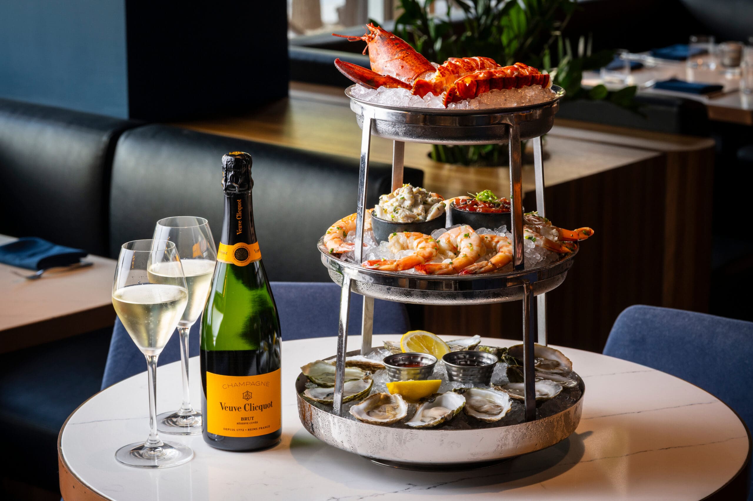 A two-tier seafood platter with oysters, prawns, lobster, and a bottle of Veuve Clicquot champagne.