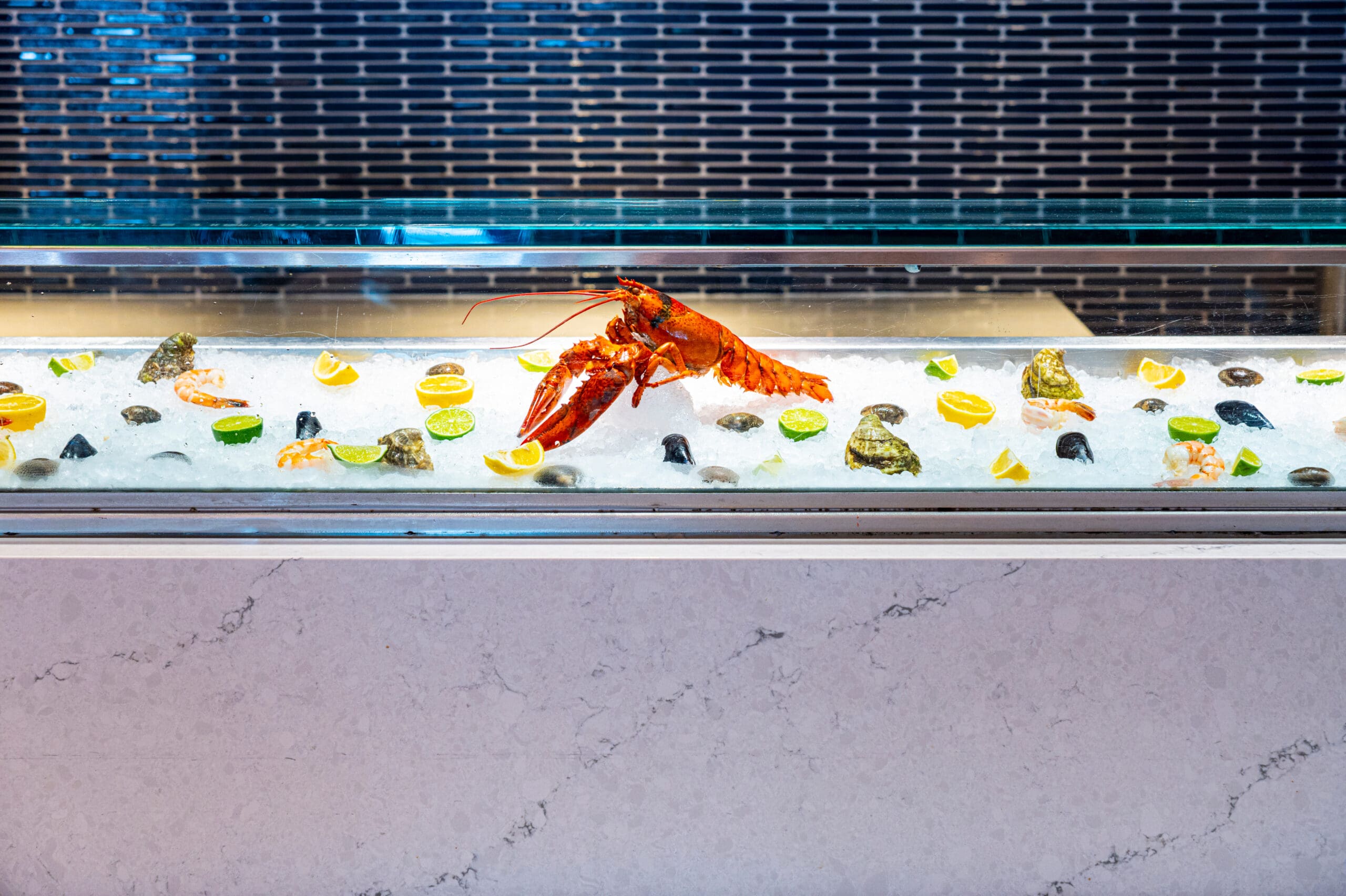 A lobster, oysters, lemon wedges, and ice are displayed in a seafood counter with a glass top.