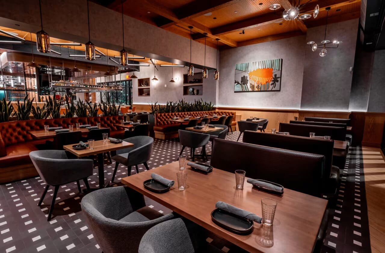 Modern restaurant interior with wooden tables, black chairs, and wall art in a warmly lit dining area.