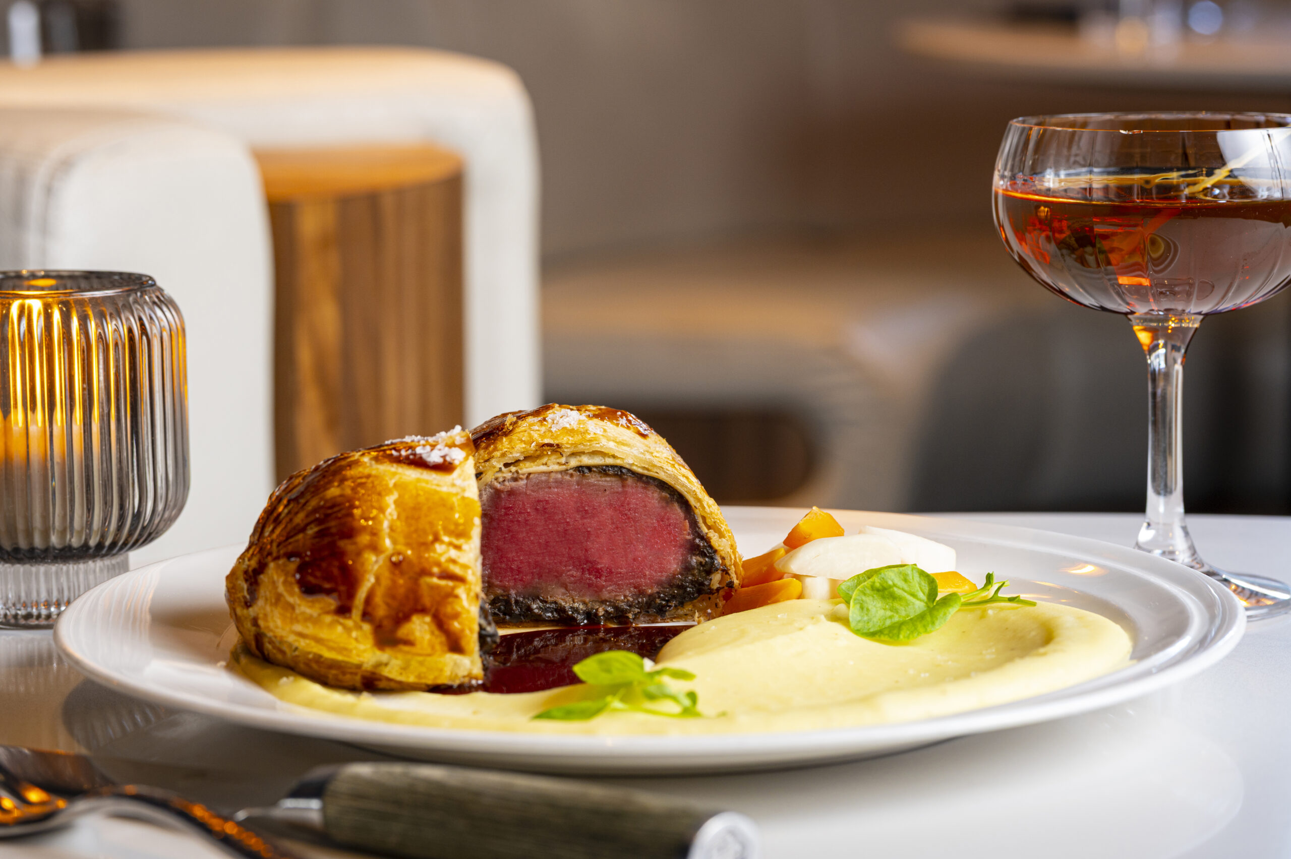 Beef Wellington served with a side of puréed potatoes and vegetables next to a glass of red wine.