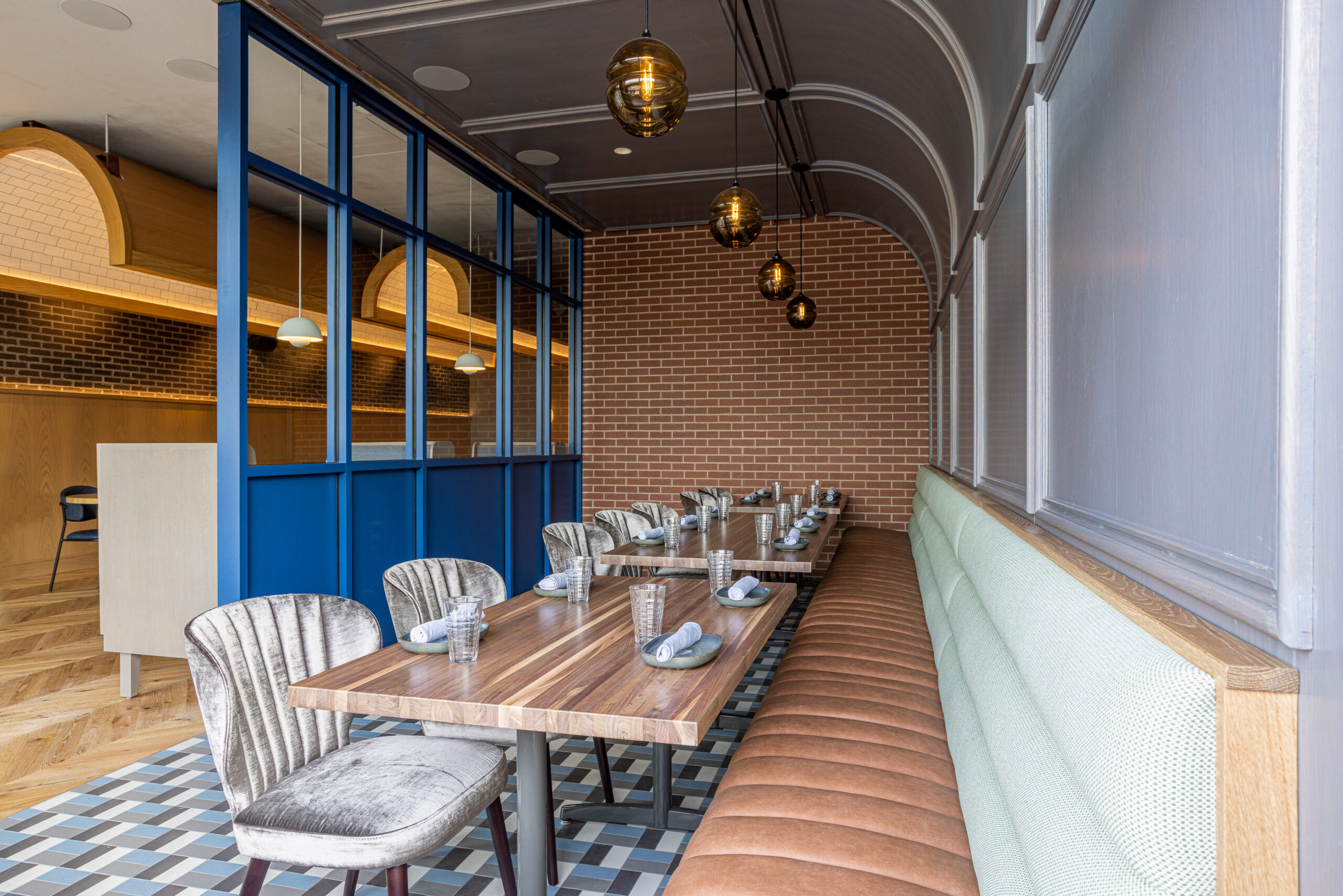 A restaurant interior featuring a wooden table with place settings, gray chairs, and a long brown leather bench.