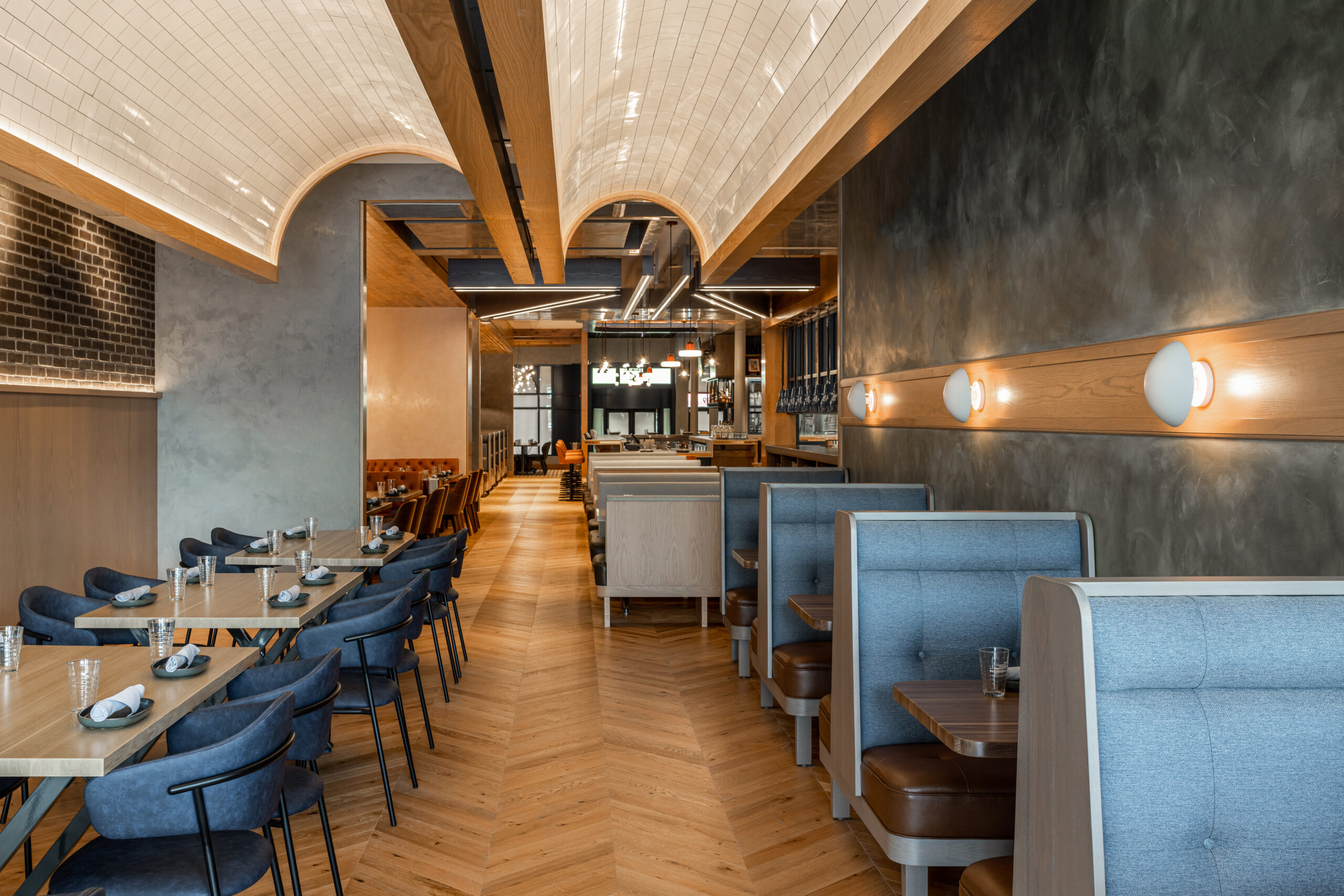 Interior of a restaurant with rows of blue booths and tables set with glasses on a wooden floor.