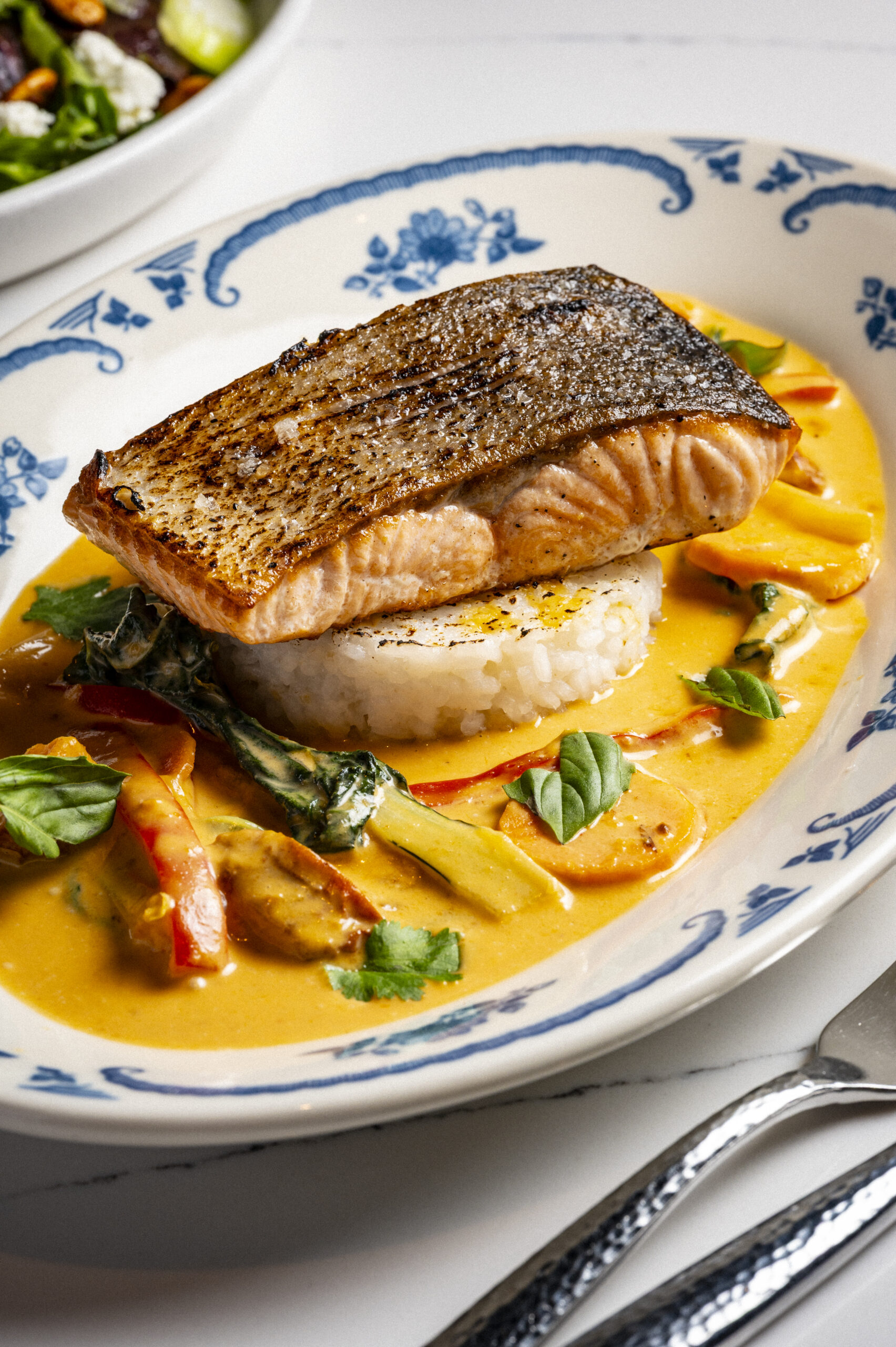Pan-seared salmon fillet over rice in a creamy curry sauce with vegetables.