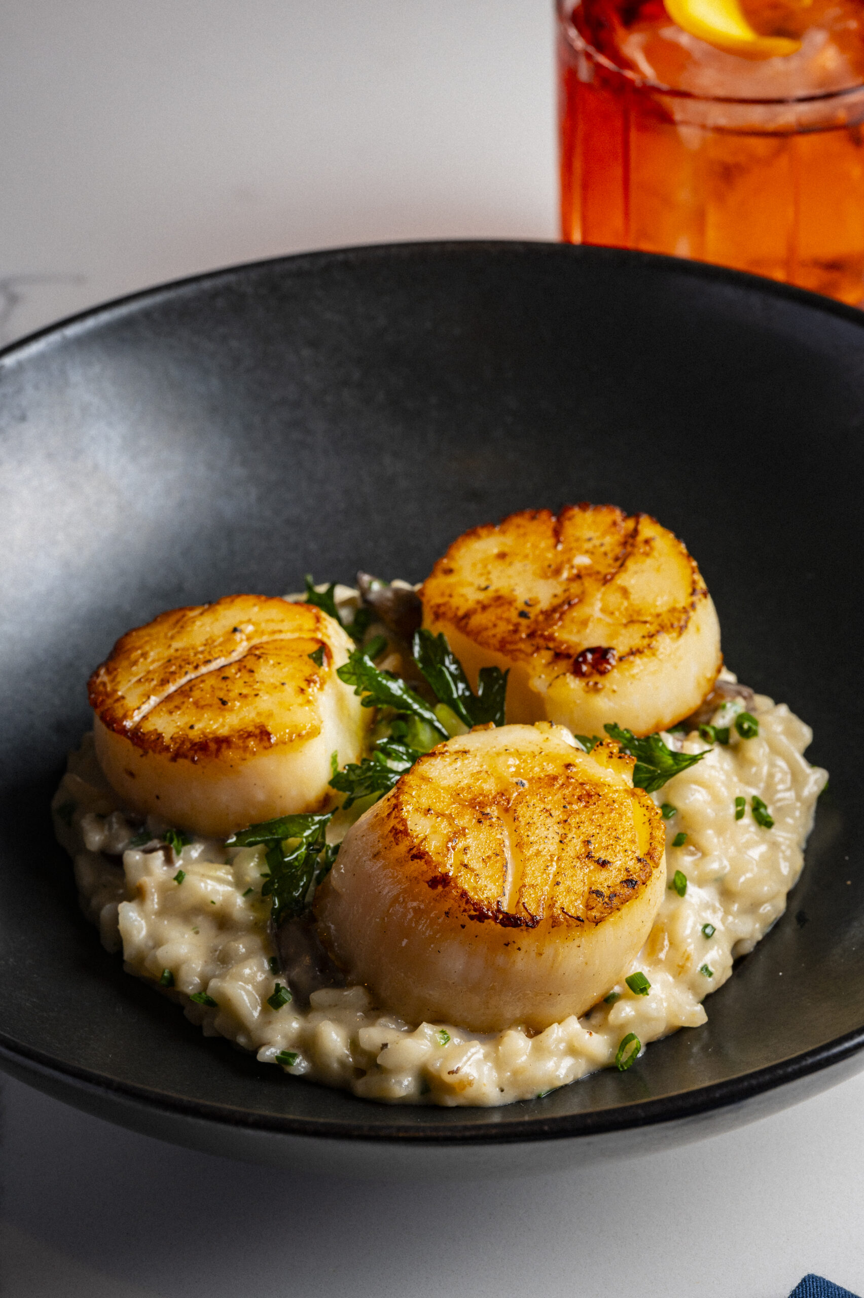 Three seared scallops served over creamy risotto in a black bowl.