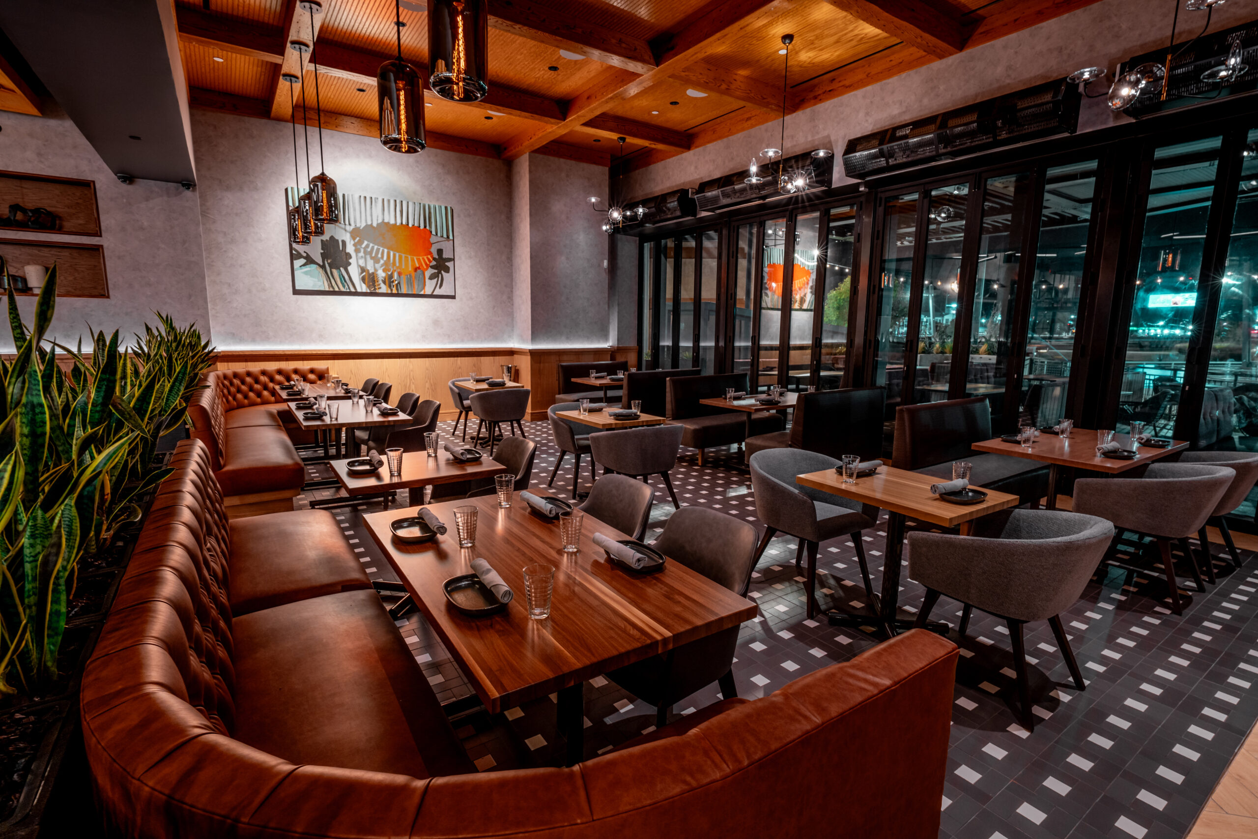 Interior of a restaurant with wooden tables, leather banquettes, and gray upholstered chairs.