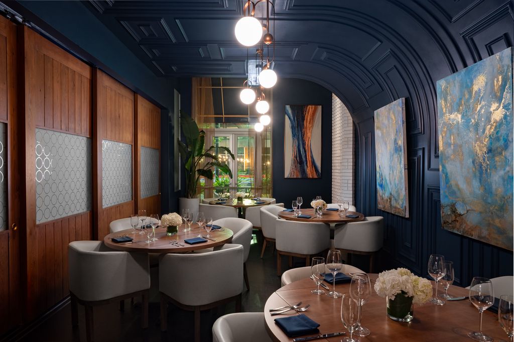 Elegant restaurant dining room with dark blue walls, circular wooden tables, and abstract art.