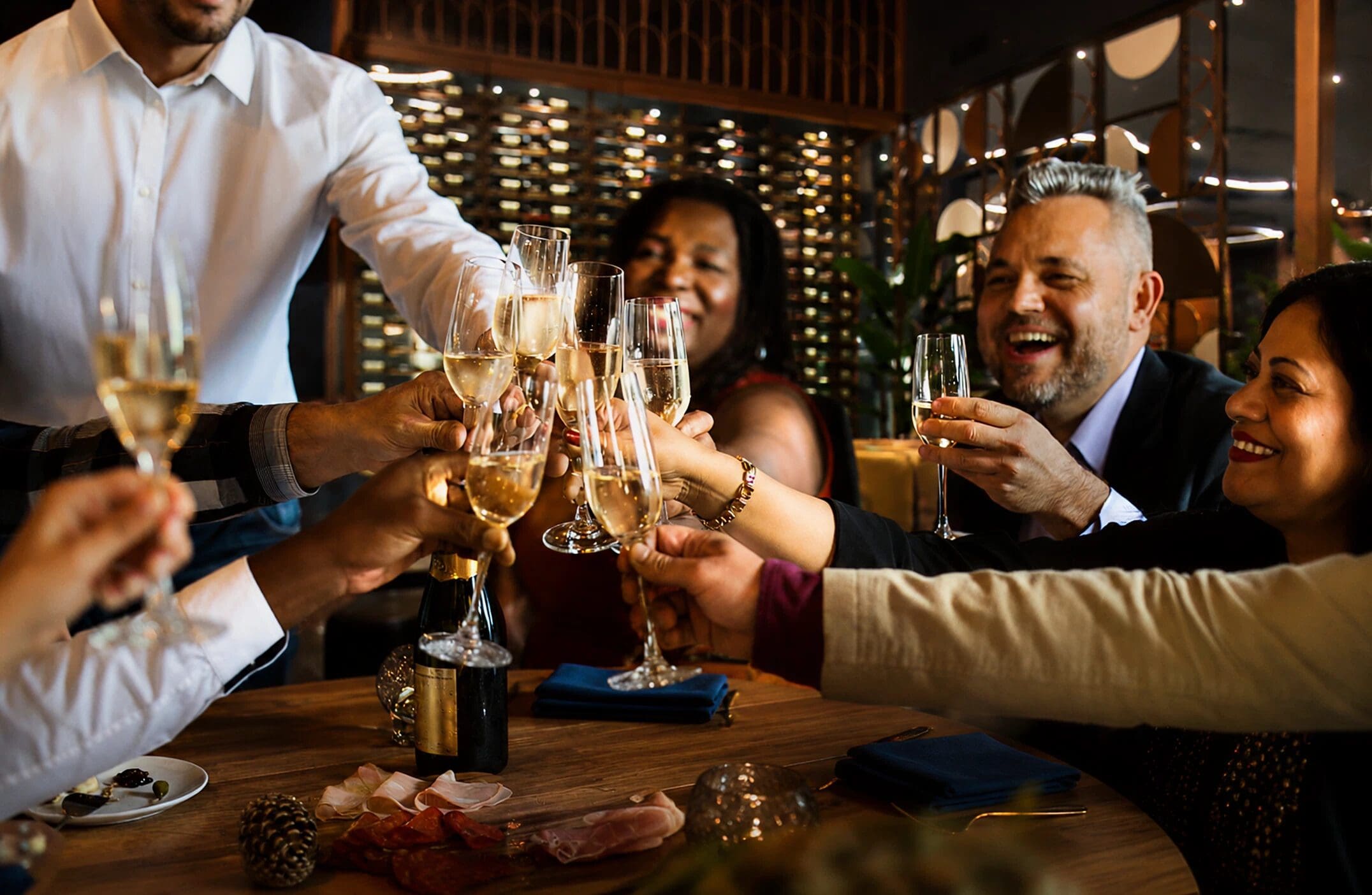 A group of people clink glasses in a celebratory toast at a restaurant table.