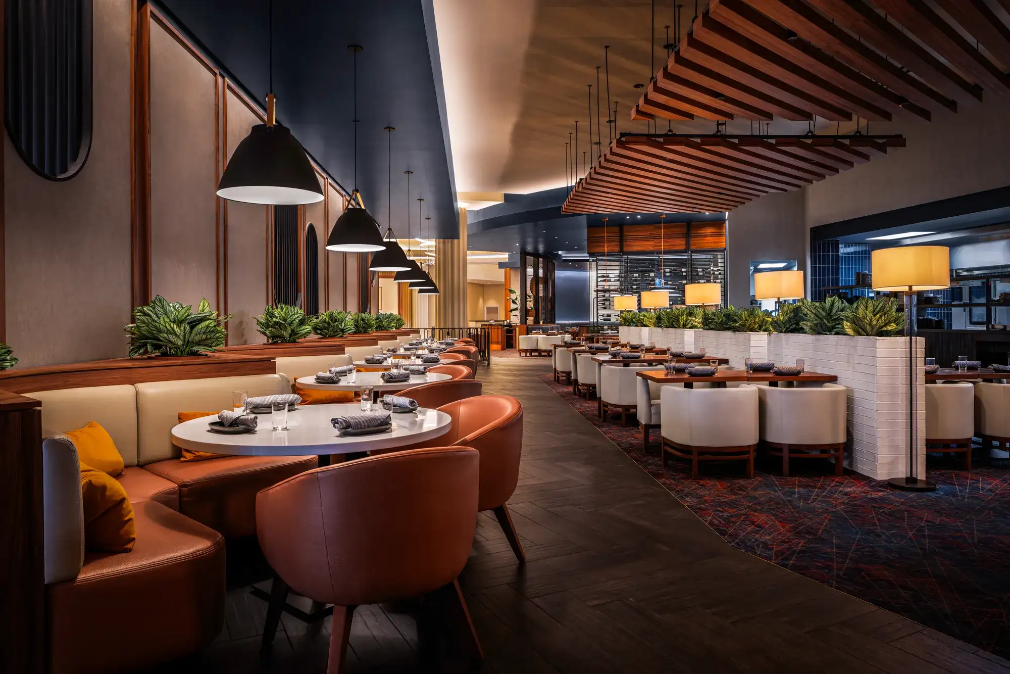 Interior of a modern restaurant featuring round tables, orange leather banquettes, and warm lighting.