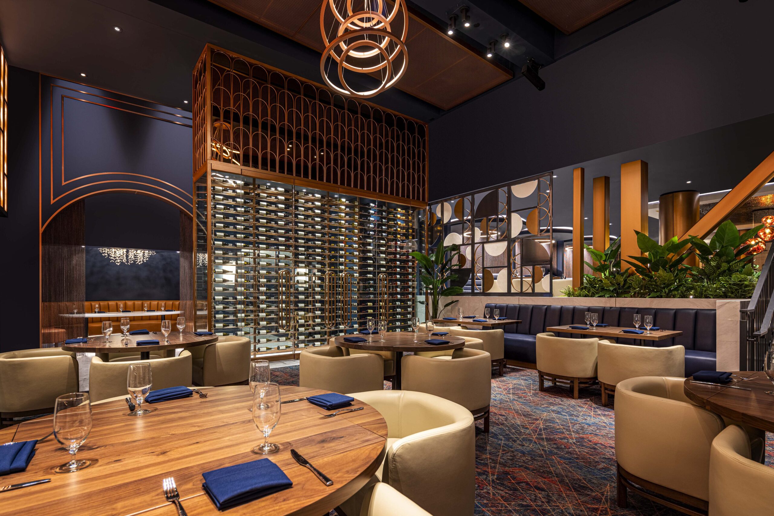 Dining room with round wooden tables, cream-coloured chairs, and a large floor-to-ceiling wine rack.