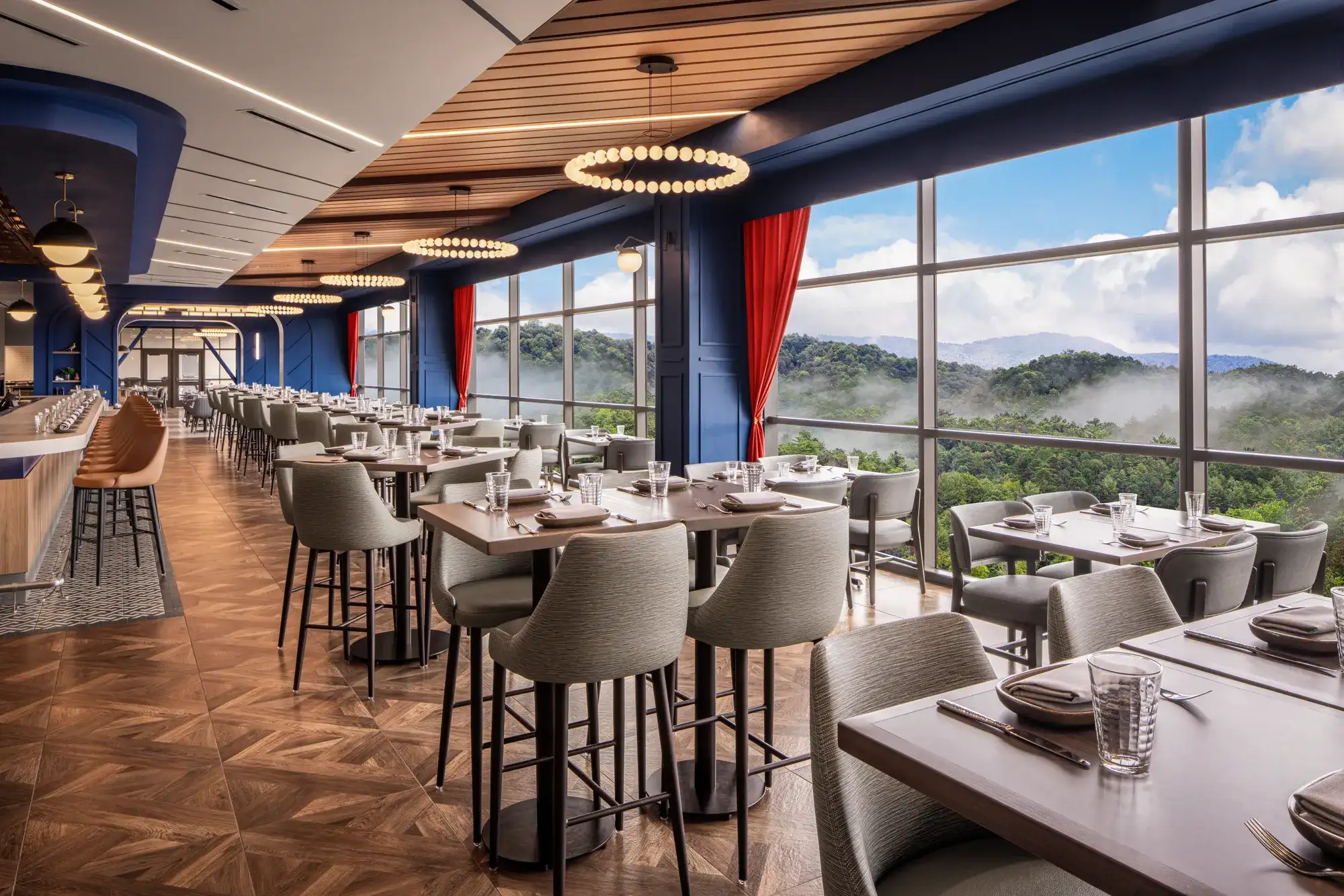 Modern restaurant interior with floor-to-ceiling windows overlooking a forest and misty mountains.