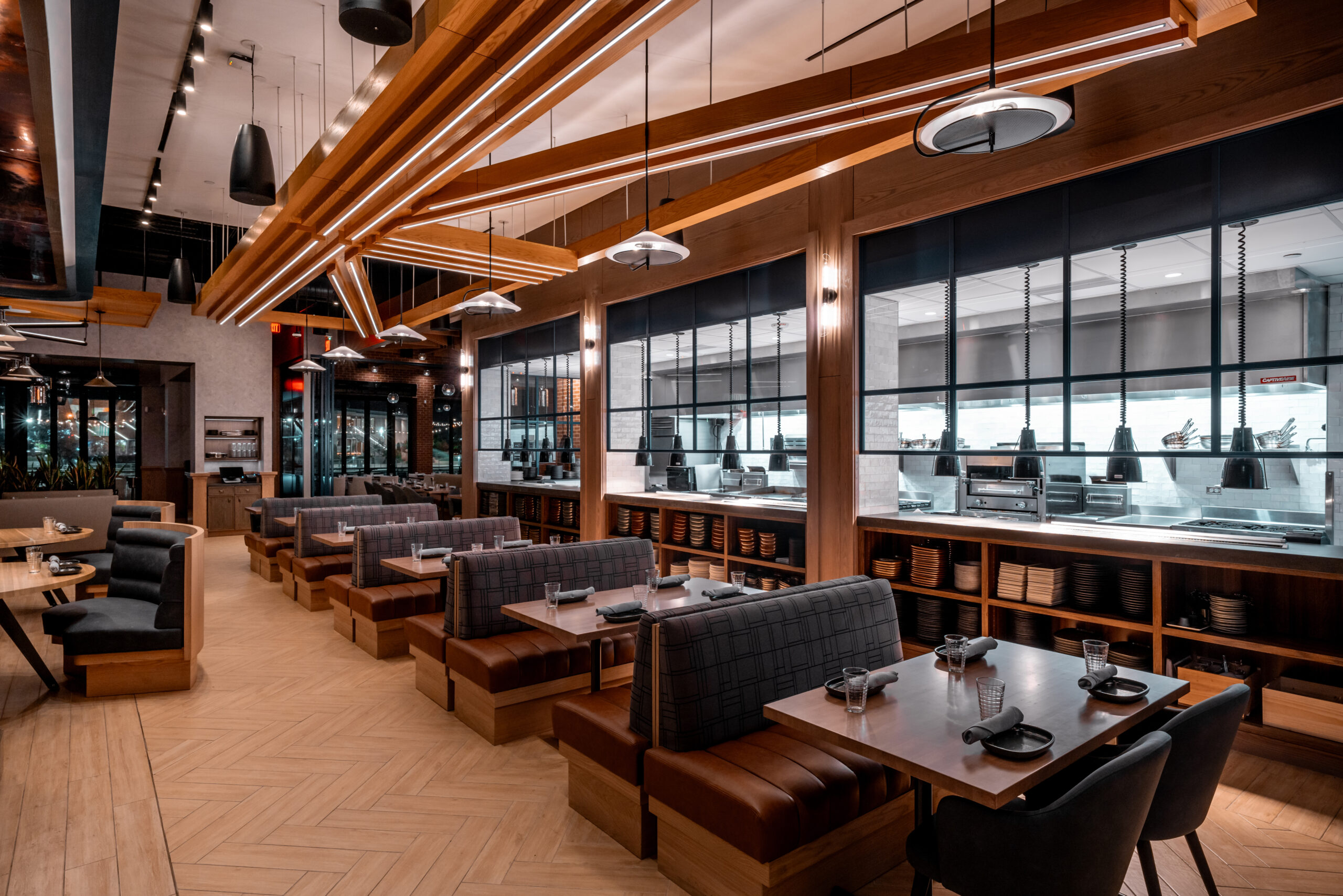 Dining room featuring rows of booths, wood-panelled ceilings, and an open kitchen view.