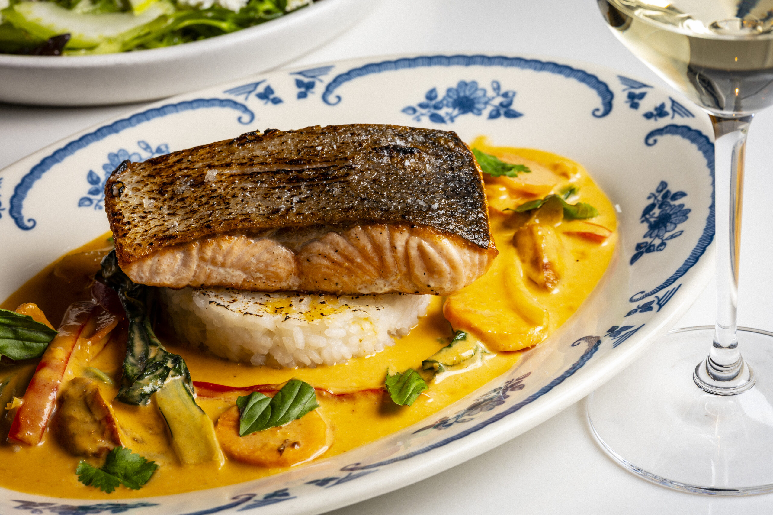 A piece of pan-seared salmon served over rice in a creamy orange sauce with vegetables.