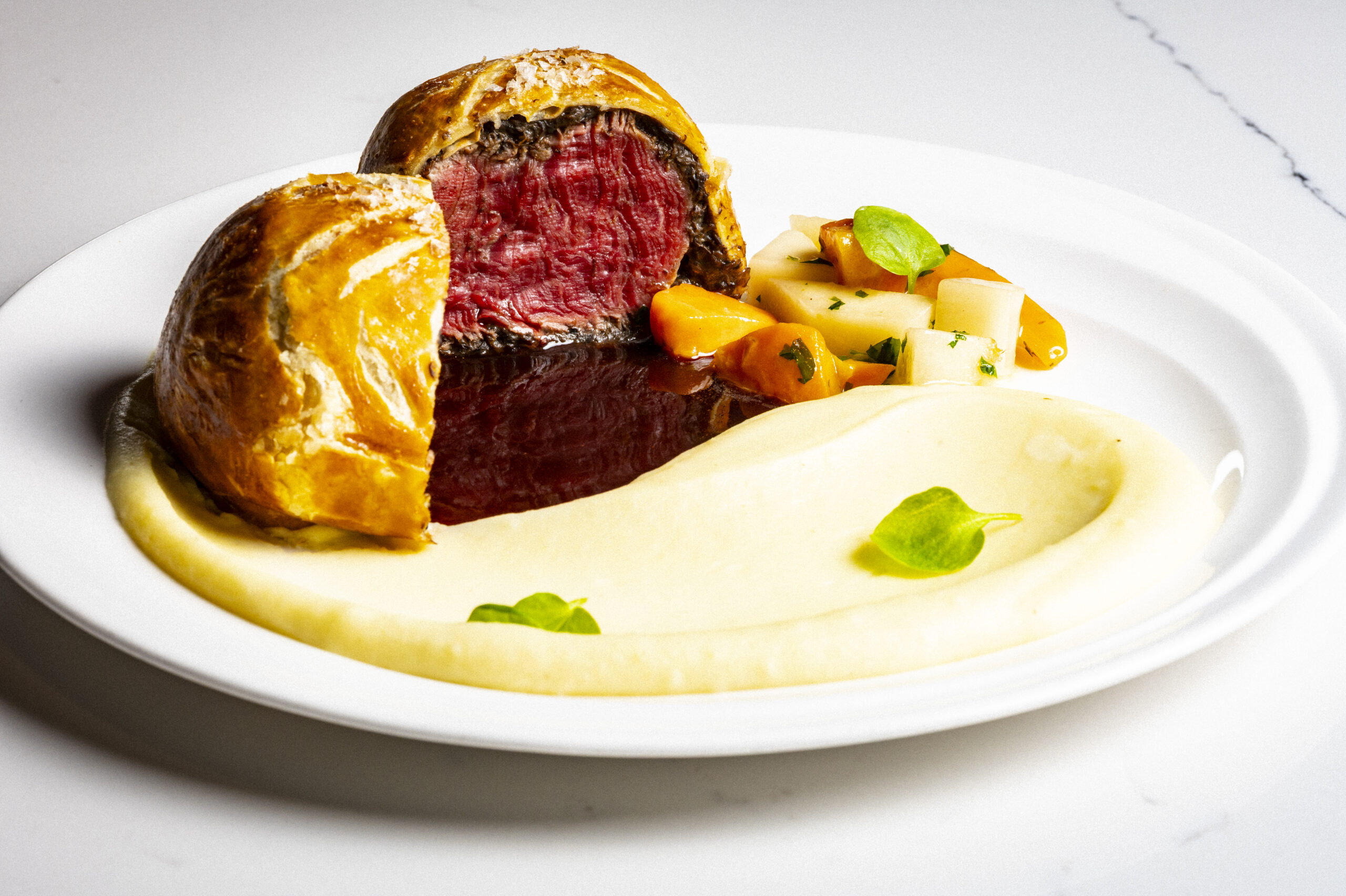 Beef Wellington served with mashed potatoes and roasted vegetables on a white plate.