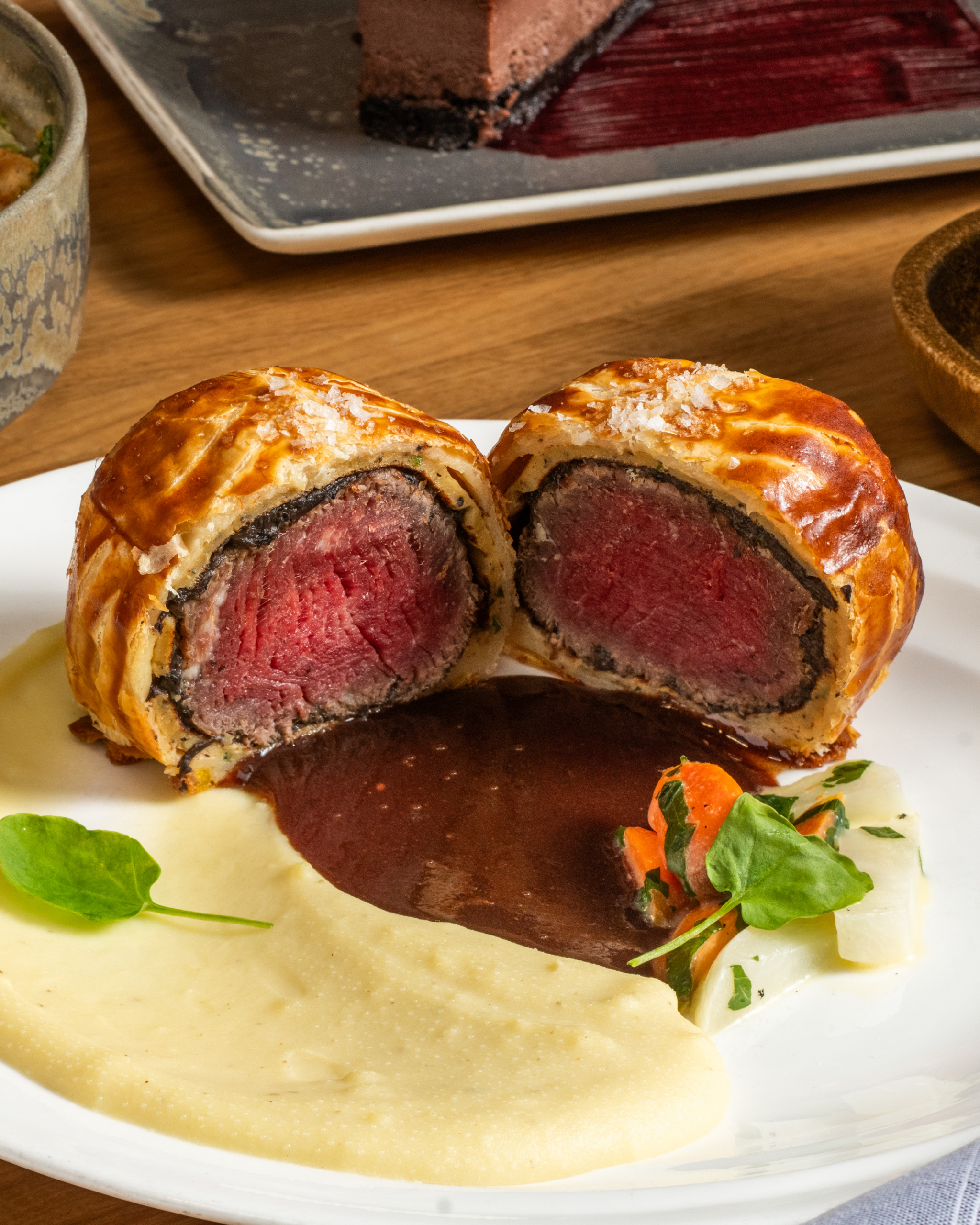 Beef Wellington cut in half on a plate with mashed potato and red wine sauce.