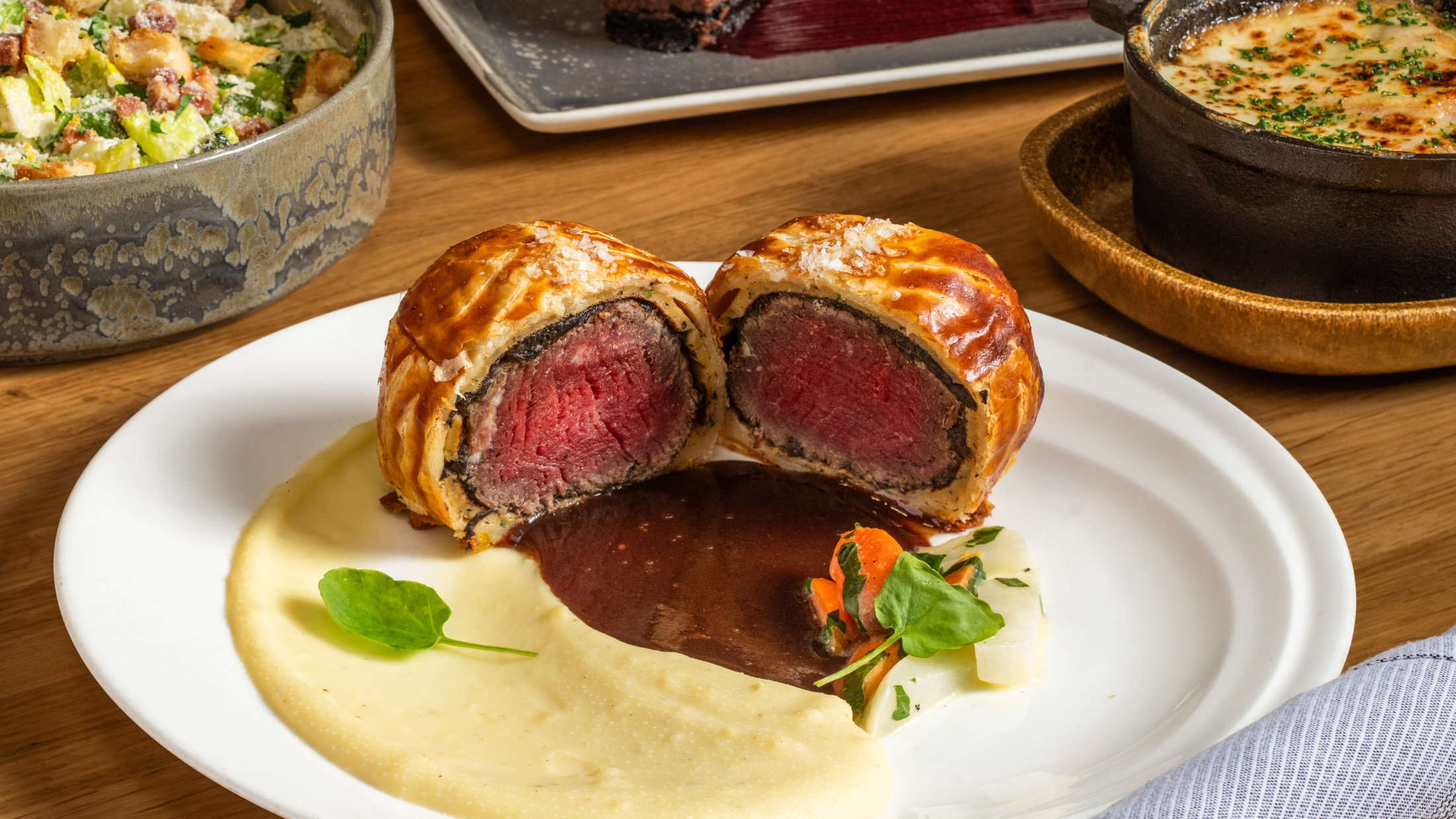 Beef Wellington cut in half on a plate with mashed potato, gravy, and vegetables.