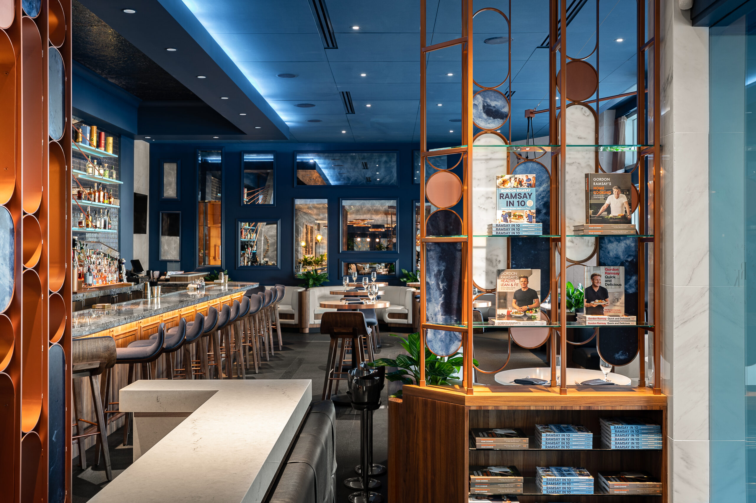 Restaurant interior with a long bar and a decorative shelving unit displaying Gordon Ramsay cookery books.