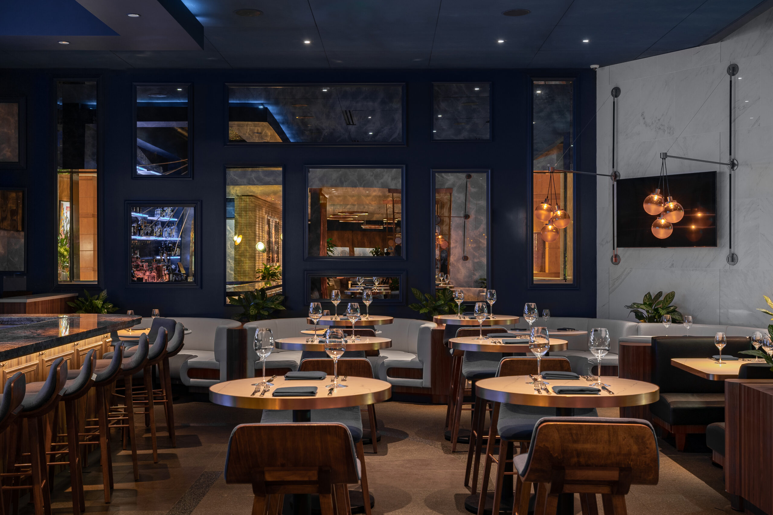 Modern restaurant interior with circular dining tables, chairs, and booths against a dark blue wall.