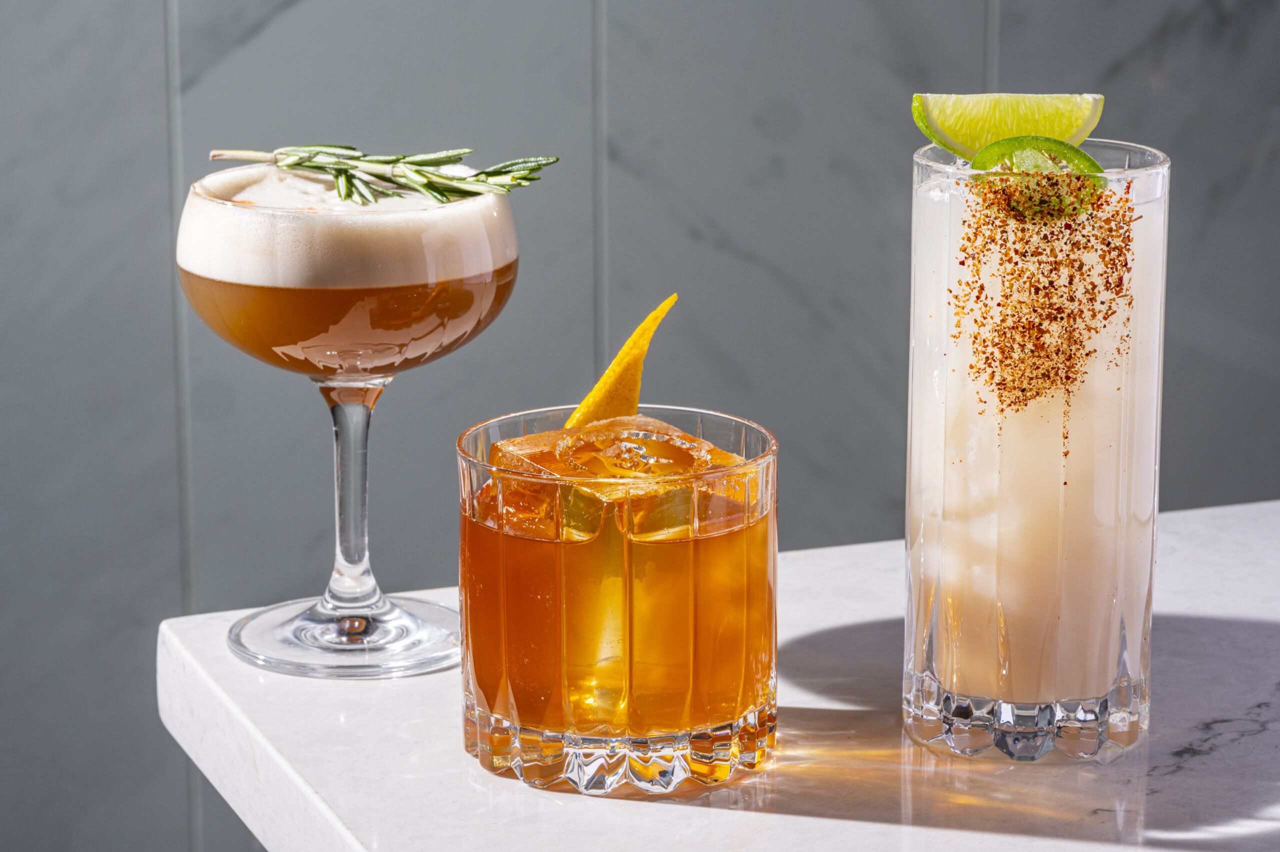 Three distinct cocktails served in different glasses on a marble surface.