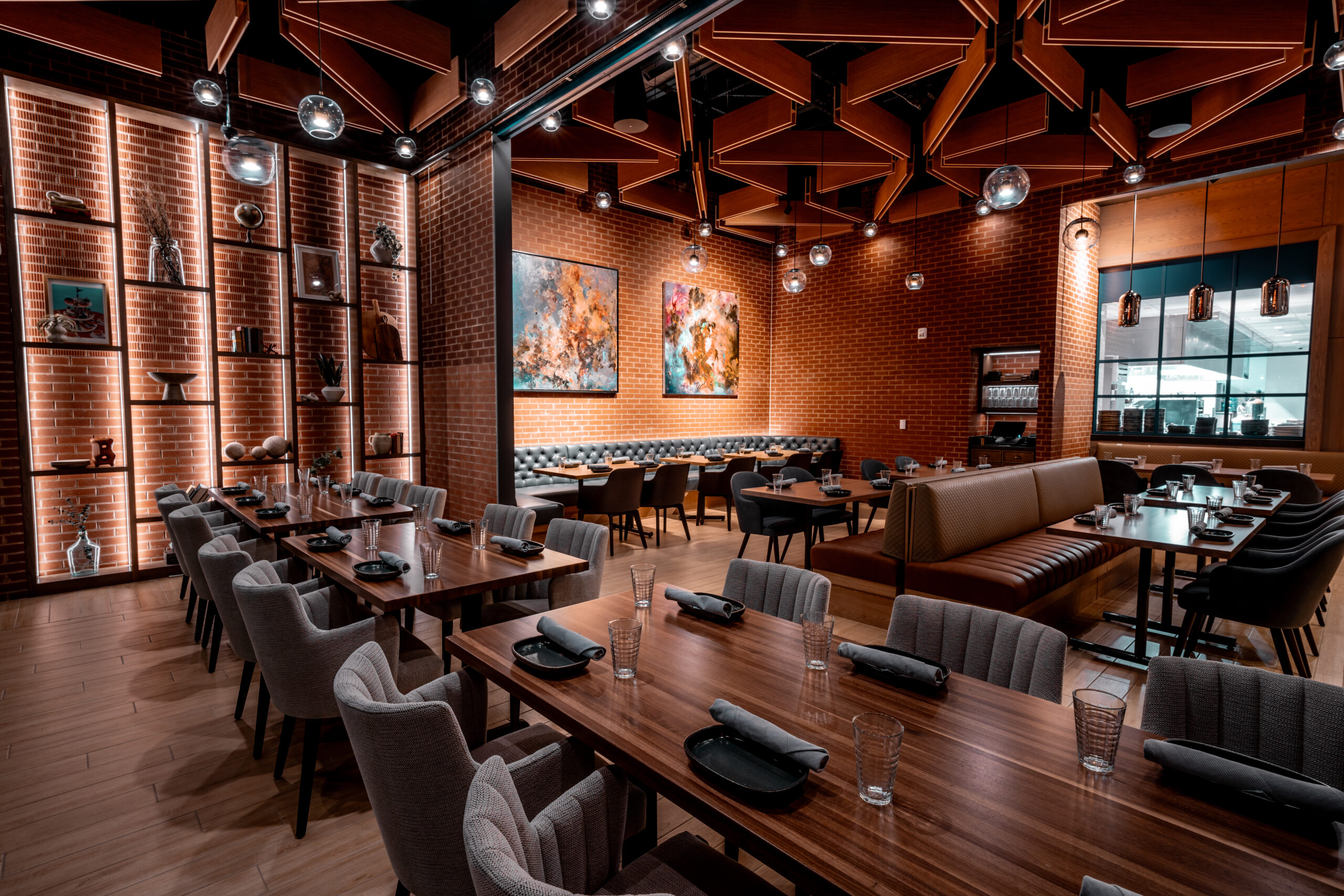 Interior of a modern restaurant with brick walls, wooden tables, and gray upholstered chairs.