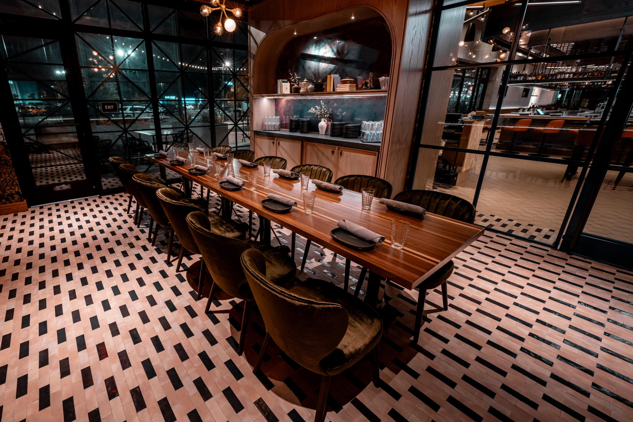 Long wooden dining table with place settings and green velvet chairs in a modern restaurant.