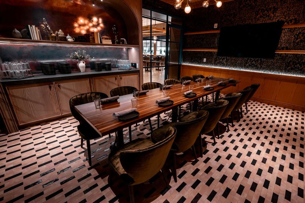 A long wooden dining table set for a group in a restaurant with a patterned tiled floor.
