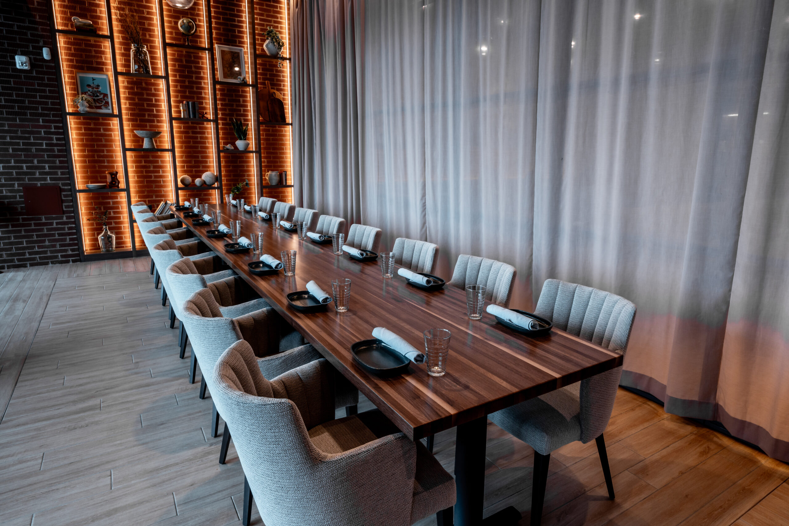 Long wooden dining table with place settings and upholstered chairs in a modern restaurant.