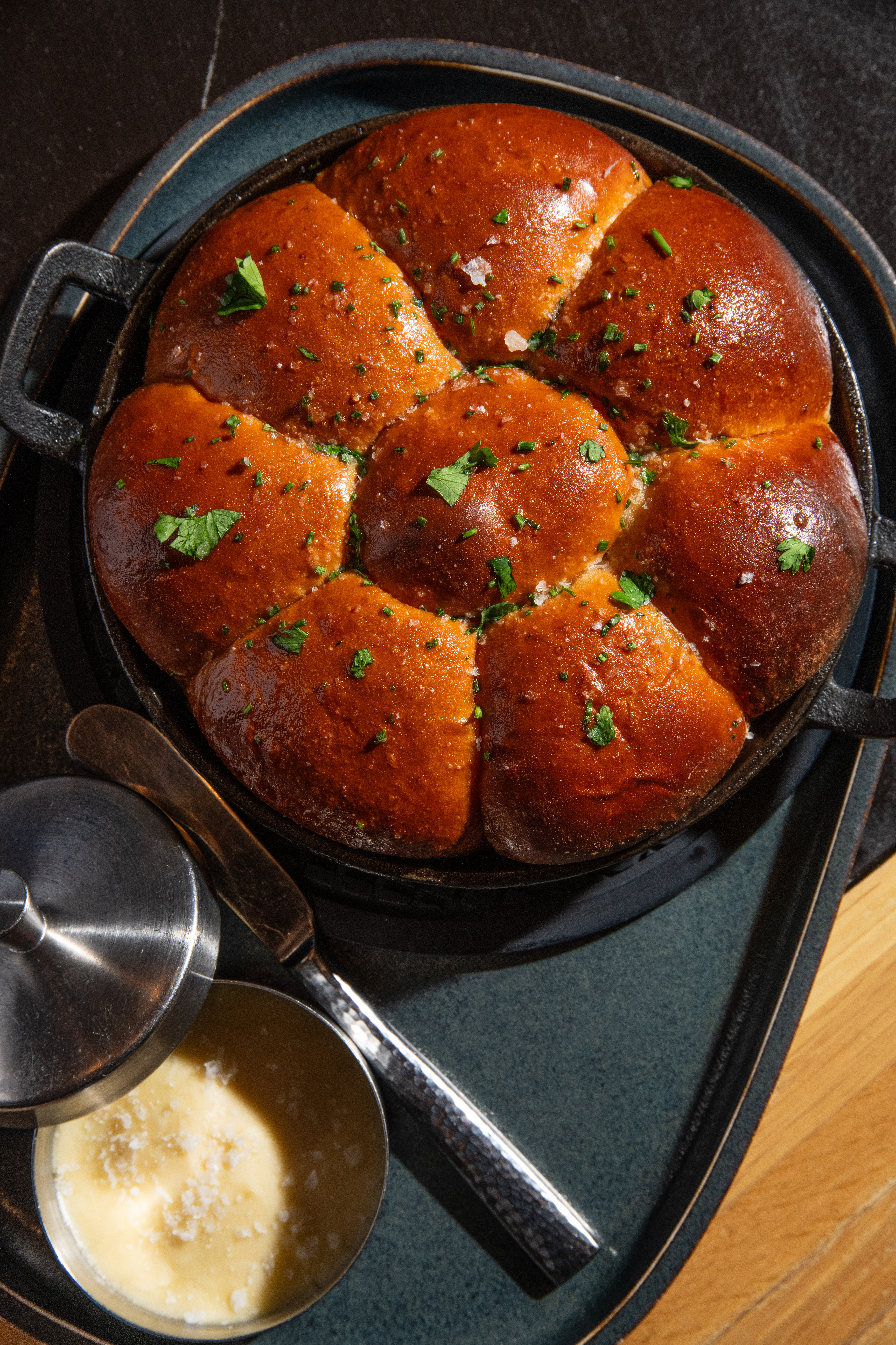 Bread rolls topped with a parsley and served in a pot with honey butter on the side