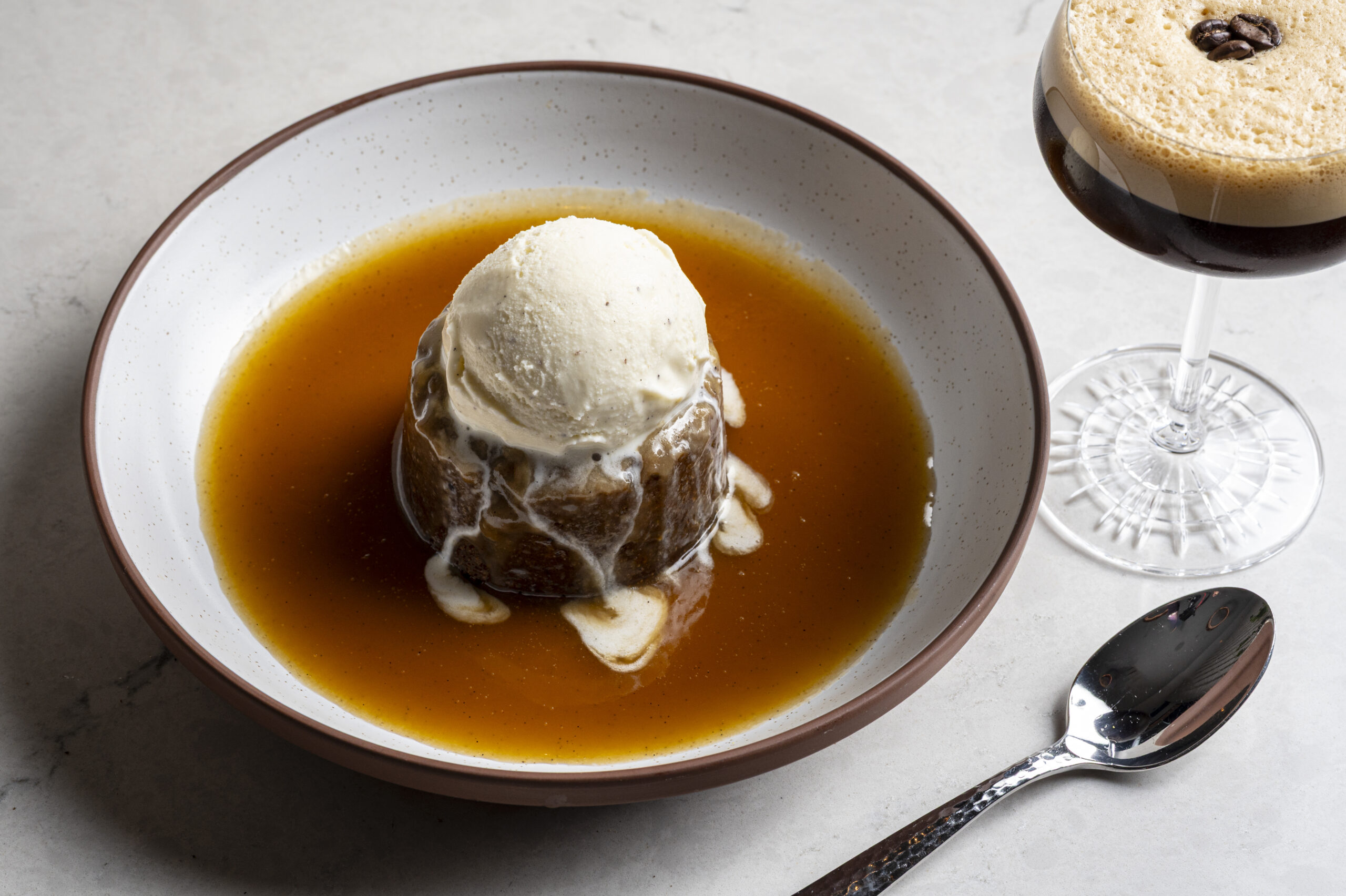 Sticky toffee pudding topped with a scoop of vanilla ice cream, served with an espresso martini and a spoon.