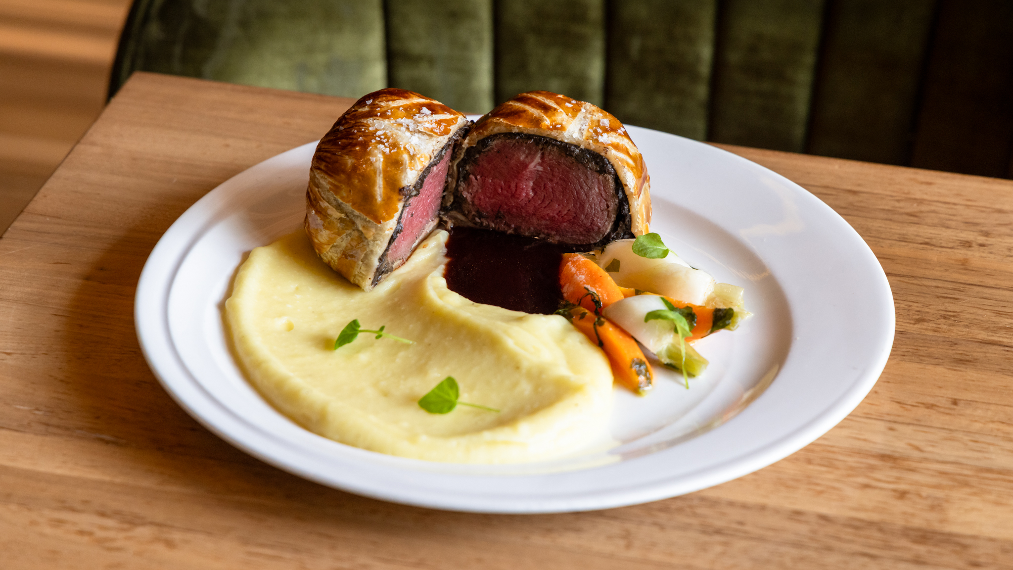 Beef Wellington served with mashed potatoes and roasted vegetables on a white plate.