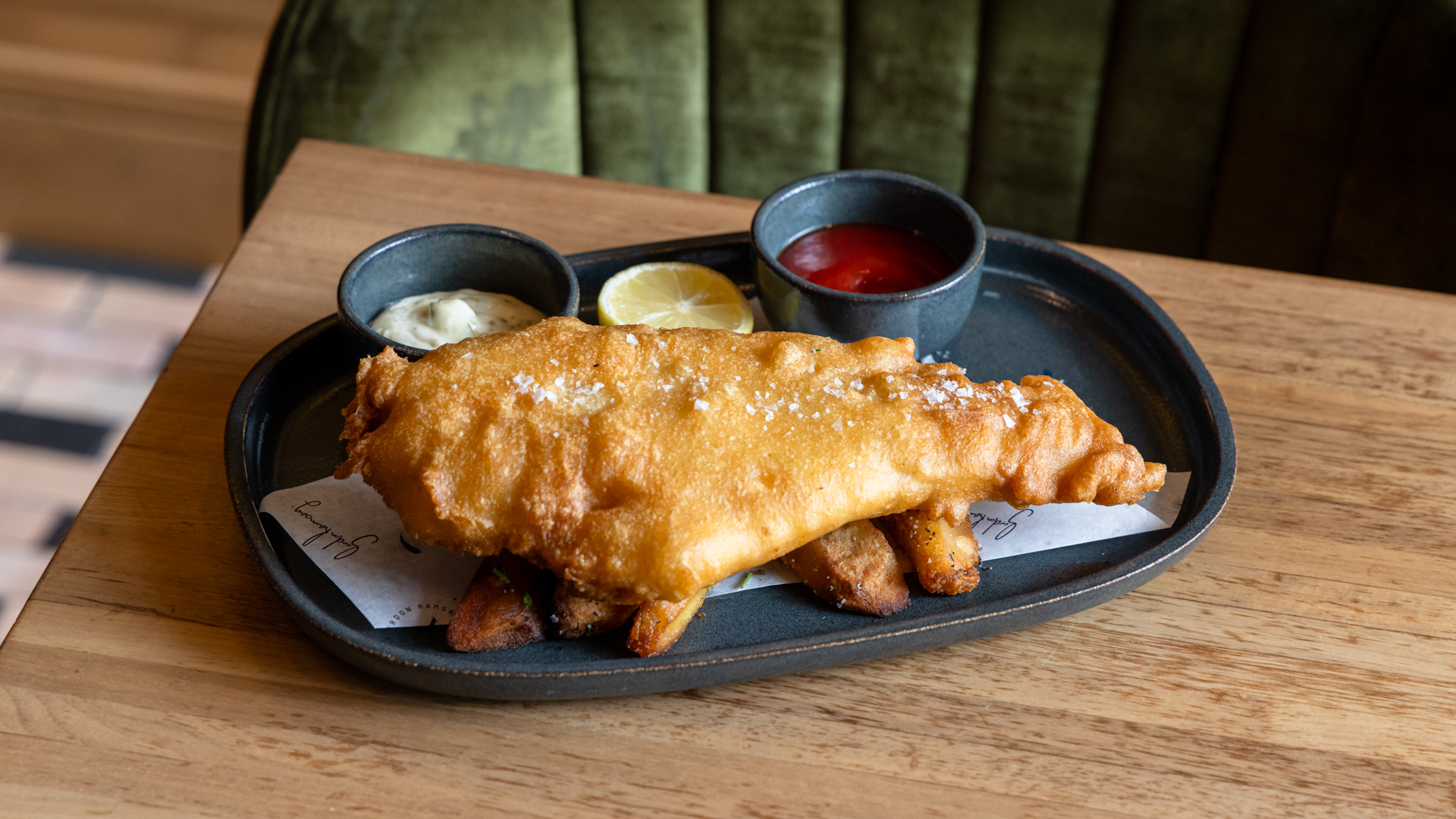 Fried fish and chips served on a platter with lemon, tartare sauce, and tomato ketchup.