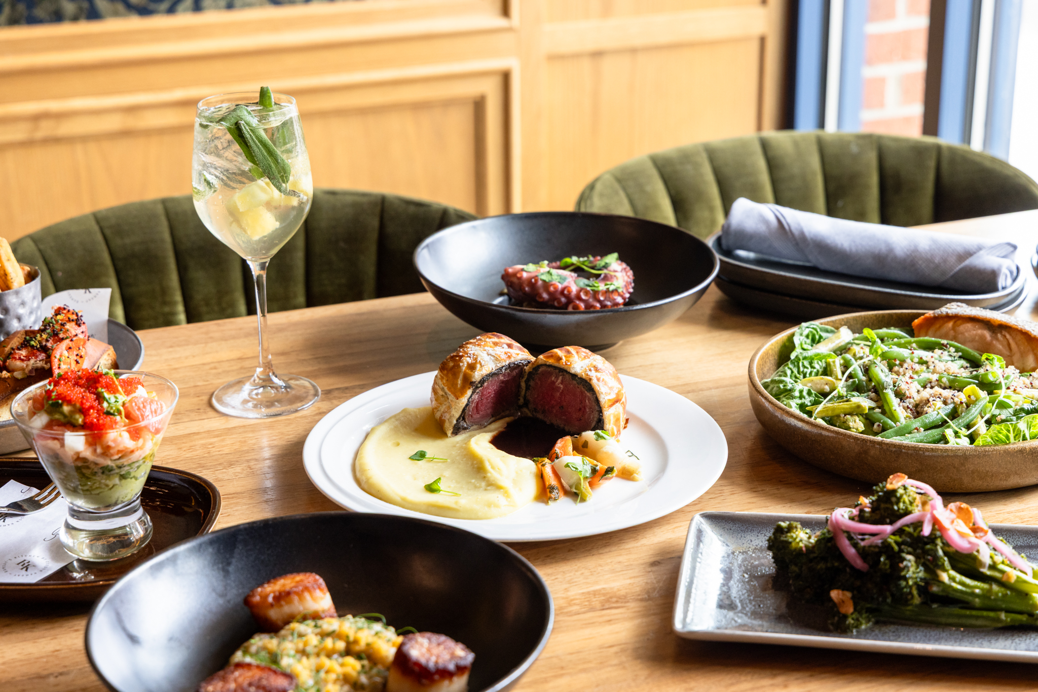 A dining table spread featuring beef Wellington with mashed potatoes, a prawn cocktail, and various vegetable sides.