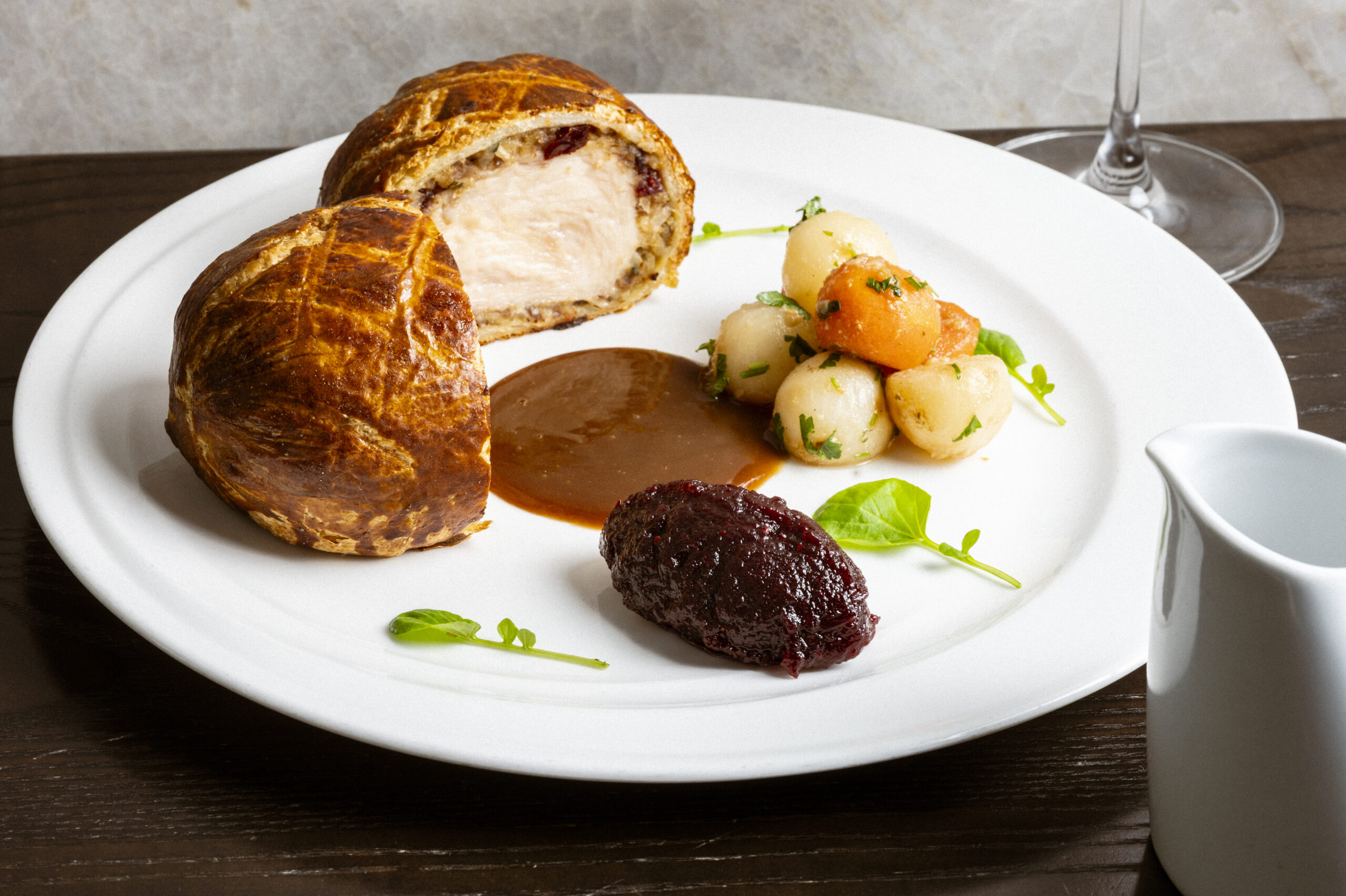 Beef Wellington served with roasted root vegetables, gravy, and a side of red relish on a white plate.